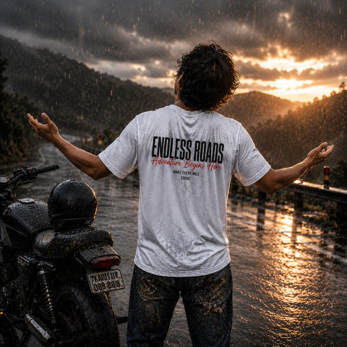 Rider in white Endless Roads oversized biker t-shirt in the rain beside a motorcycle.